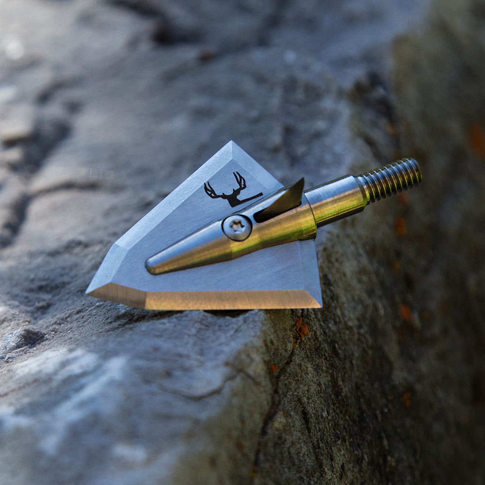 broadhead with mule deer engraving on it on top of a rock