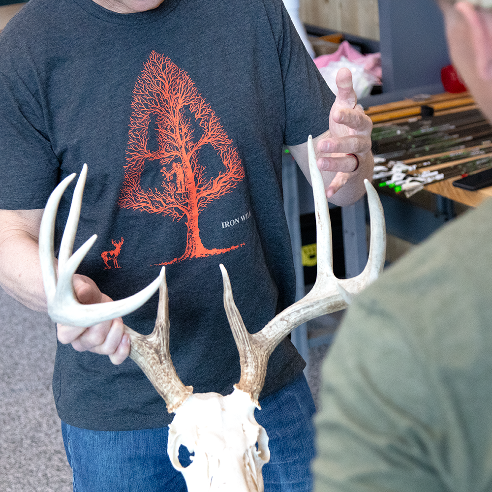 showing off a whitetail buck while wearing a tree ambush shirt in a bow shop