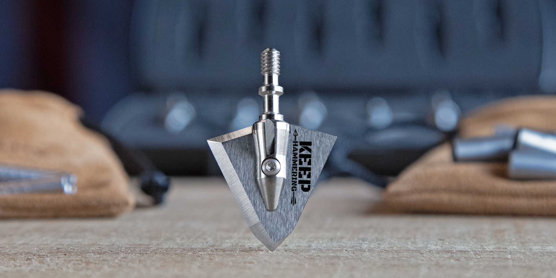 keep hammering broadhead pointed into a table with accessories in the background